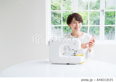 スマホを見ながらでミシンを操作する女性 スマホを見ながらでミシンを操作する女性 84831635
