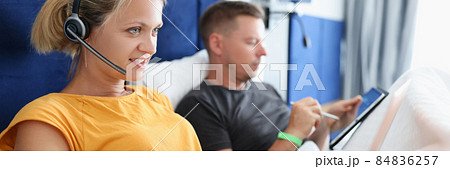 Woman in headphones lying in bed and working at laptop next to man with tablet Woman in headphones lying in bed and working at laptop next to man with tablet 84836257