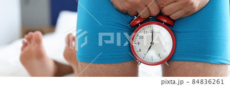Man holding alarm clock near genitals against background of lying female legs closeup Man holding alarm clock near genitals against background of lying female legs closeup 84836261