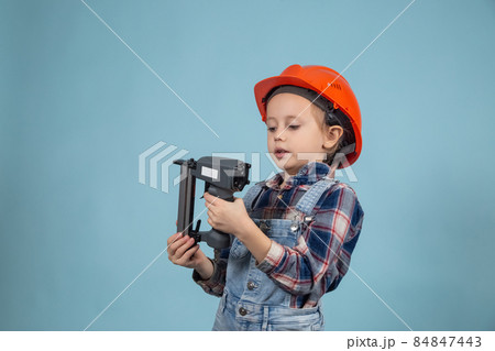 Adorable child is wearing safety helmet,holding construction stapler at hands. 84847443