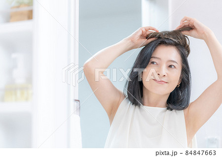 鏡に映った部分かつらを頭に乗せようとするミドル女性の頭のアップ 鏡に映った部分かつらを頭に乗せようとするミドル女性の頭のアップ 84847663