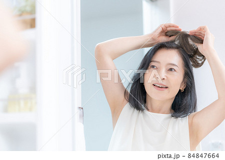 鏡に映った部分かつらを頭に乗せようとするミドル女性の頭のアップ 84847664