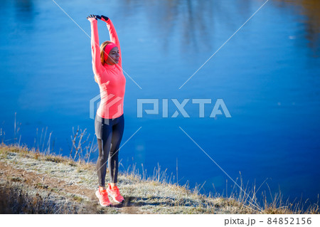 Young slim fitness woman stretching near lake before jogging in the frosty morning. Young slim fitness woman stretching near lake before jogging in the frosty morning. 84852156