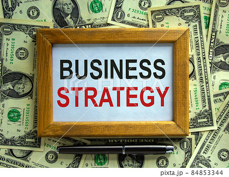 Wooden picture frame with inscription 'business strategy' on beautiful background from dollar bills and metalic pen. Business concept. Wooden picture frame with inscription 'business strategy' on beautiful background from dollar bills and metalic pen. Business concept. 84853344
