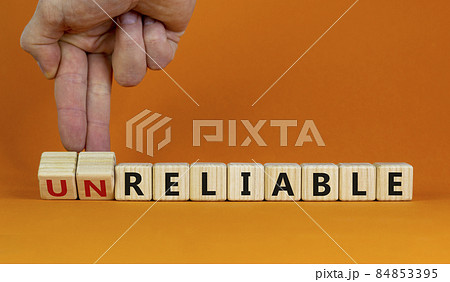 Unreliable or reliable symbol. Businessman turns wooden cubes and changes the word unreliable to reliable. Beautiful orange background, copy space. Business and unreliable or reliable concept. 84853395