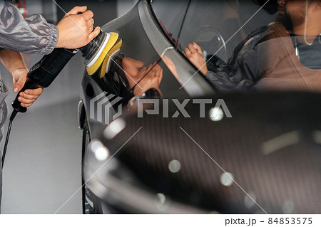 Worker polishing car with special grinder and wax from scratches at the car service station. Professional car detailing and maintenance concept 84853575