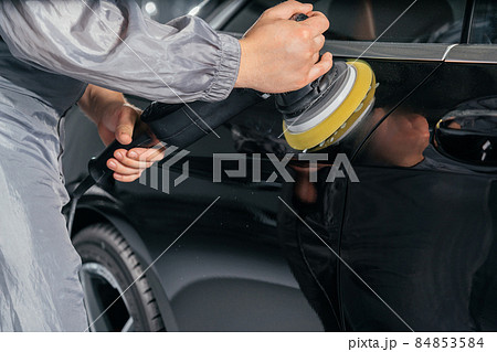Worker polishing car with special grinder and wax from scratches at the car service station. Professional car detailing and maintenance concept 84853584