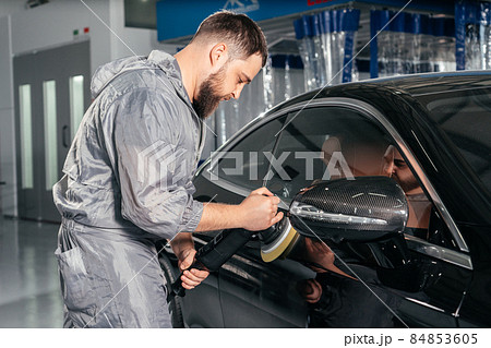 Worker polishing car with special grinder and wax from scratches at the car service station. Professional car detailing and maintenance concept Worker polishing car with special grinder and wax from scratches at the car service station. Professional car detailing and maintenance concept 84853605