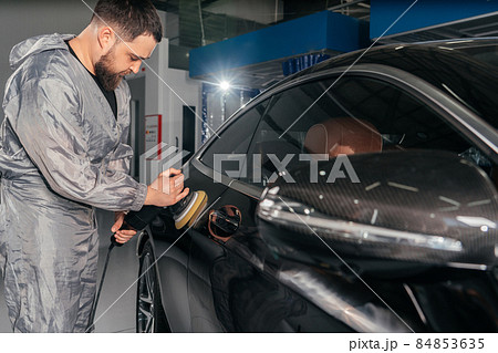 Worker polishing car with special grinder and wax from scratches at the car service station. Professional car detailing and maintenance concept 84853635