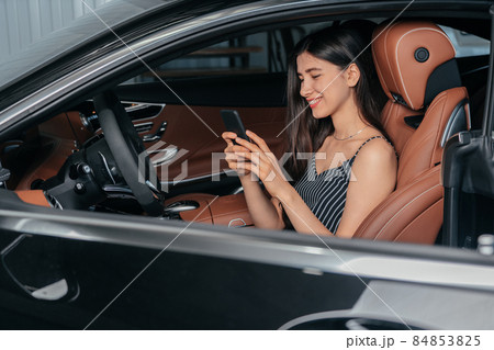 Young attractive asian woman using phone while sitting in a luxury car front sea Young attractive asian woman using phone while sitting in a luxury car front sea 84853825