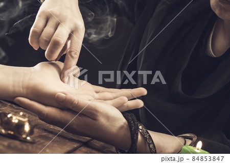The witch is a fortune teller reading a good luck close-up. The fortune teller draws lines on the client's hand 84853847
