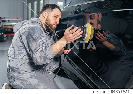 Worker polishing car with special grinder and wax from scratches at the car service station. Professional car detailing and maintenance concept Worker polishing car with special grinder and wax from scratches at the car service station. Professional car detailing and maintenance concept 84853921
