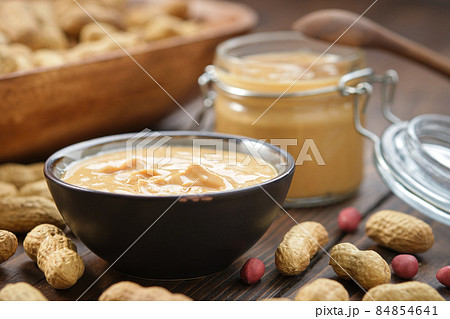 Bowl of peanut paste and fresh nuts. Jar of raw organic peanut butter on background. 84854641