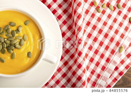 Pumpkin soup with cream and pumpkin seeds. background with red fabric. Free space, closeup. Flat lay. 84855576