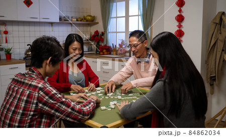 asian family of four shuffling tiles while playing mahjong together on chinese lunar new year's eve at home. chinese word at background translation: luck 84862034