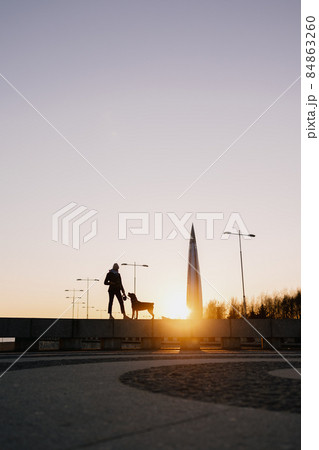 woman walking her dog at sunset, beautiful sunset against the background of modern buildings 84863260