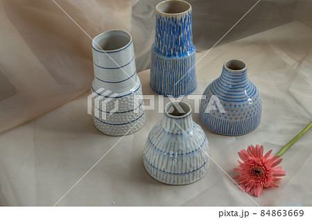 Four Blue and White handmade ceramic vase with Pink flower on Blush textured table cloth. Four Blue and White handmade ceramic vase with Pink flower on Blush textured table cloth. 84863669