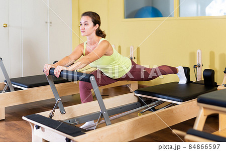 Young woman doing pilates exercises with reformer bed 84866597