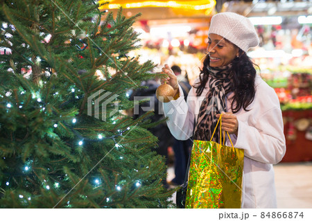 Latin woman decorating christmas tree outdoors Latin woman decorating christmas tree outdoors 84866874