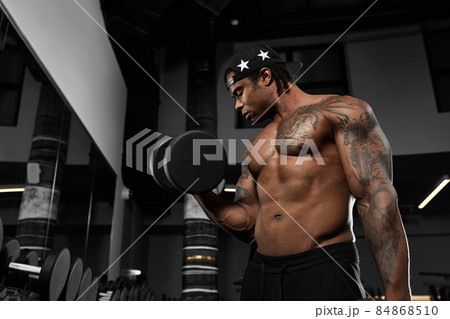 Strong and muscular dark skin man trains on modern equipment in gym. Portrait of muscular pumped up fitness trainer 84868510