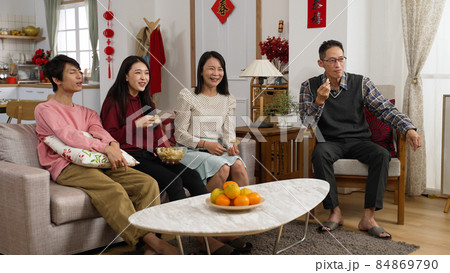 family eating snacks together at home during spring festival and watching a boring tv show chosen by the happy mother who's talking with gestures. chinese text translation: spring and congratulation family eating snacks together at home during spring festival and watching a boring tv show chosen by the happy mother who's talking with gestures. chinese text translation: spring and congratulation 84869790
