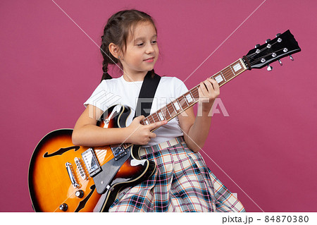 A young girl in a school uniform plays an electric guitar 84870380