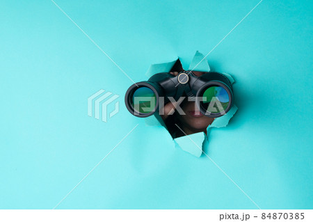 Female hand holds black binoculars on a blue background. Journey, find and search concept. Banner. 84870385