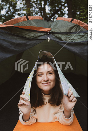 A female tourist fools around with a map in a tent in the woods. Fun in the camp 84870884