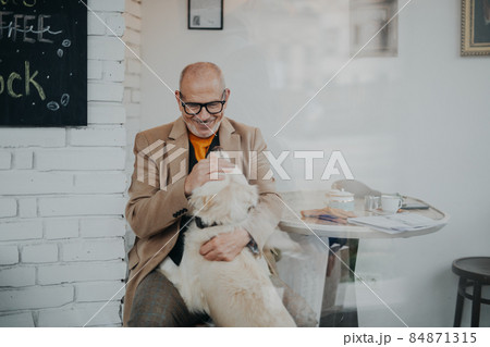 Happy senior man sitting in cafeteria and playing with his dog, shot through glass. 84871315