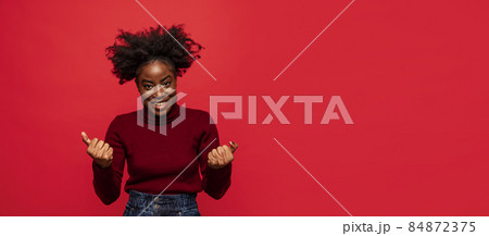 Pleased African young girl showing her fists as symbol of win, success isolated on dark red background. Pleased African young girl showing her fists as symbol of win, success isolated on dark red background. 84872375
