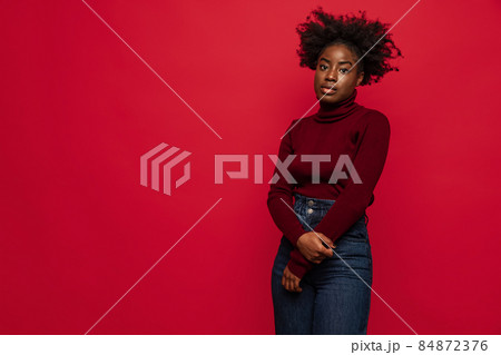 Half-length portrait of young African woman in warm casual style clothes isolated on red background. Concept of emotions Half-length portrait of young African woman in warm casual style clothes isolated on red background. Concept of emotions 84872376