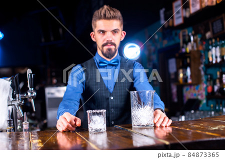 Confident barman makes a cocktail while standing near the bar counter in nightclub Confident barman makes a cocktail while standing near the bar counter in nightclub 84873365