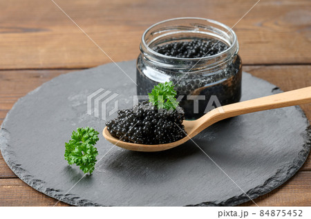 fresh grainy black paddlefish caviar in brown wooden spoon on a brown table, close up 84875452