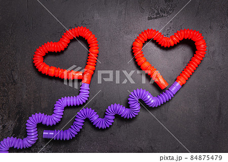 Tube toys bent as two red heart balloons and wavy ribbons on black background Tube toys bent as two red heart balloons and wavy ribbons on black background 84875479