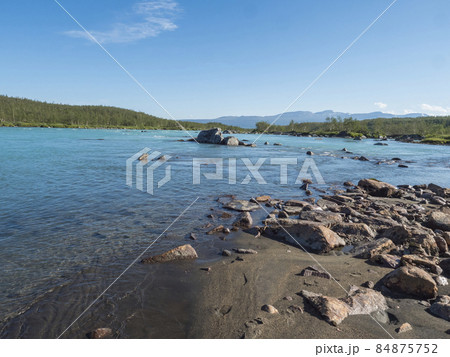 View of turquoise blue water of wild Vuojatadno river. Northern landscape in Swedish Lapland with birch tree forest and green mountains at Padjelantaleden hiking trail. Summer sunny day, blue sky 84875752