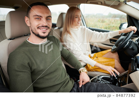 Portrait of smiling man in interior of automobile. Bearded guy travelling by vehicle with beautiful female blonde who driving auto. Young couple people with happy face expression riding in elite car. Portrait of smiling man in interior of automobile. Bearded guy travelling by vehicle with beautiful female blonde who driving auto. Young couple people with happy face expression riding in elite car. 84877392