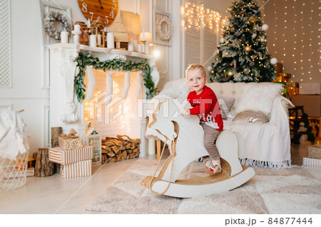 cute little boy on rocking horse in room with fireplace and christmas tree. 84877444