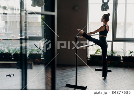 Slim ballerina during her stretch routine next on ballet barre in studio 84877689