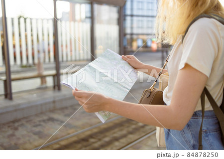 Young blonde female tourist traveler looking for the right direction on a trip map at the bus stop on a city street, traveling in Europe. Tourism, destination concept Young blonde female tourist traveler looking for the right direction on a trip map at the bus stop on a city street, traveling in Europe. Tourism, destination concept 84878250