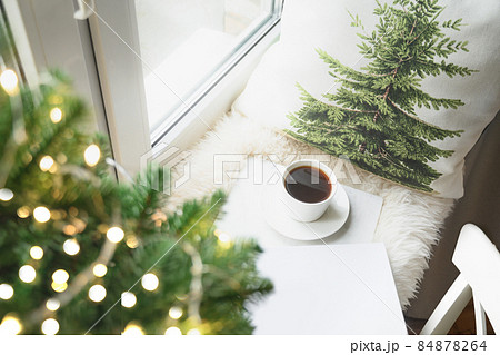 Winter coffee on window sill with Christmas tree and pillow for cozy reading. Winter coffee on window sill with Christmas tree and pillow for cozy reading. 84878264