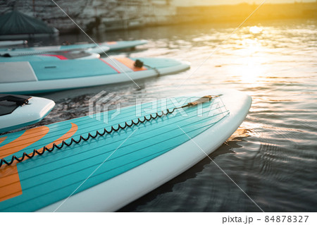 Close up stand up paddle board SUP on lake with water lilies, paddling in summer time on dark blue water at sunset Close up stand up paddle board SUP on lake with water lilies, paddling in summer time on dark blue water at sunset 84878327