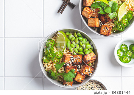 Vegan noodles ramen soup with marinated tofu, edamame beans and hot peppers in gray bowls. Vegan noodles ramen soup with marinated tofu, edamame beans and hot peppers in gray bowls. 84881444