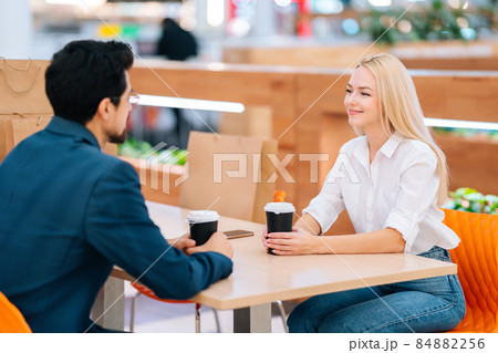 Happy handsome bearded man and attractive blonde woman having date sitting at table in mall, blurred background. 84882256