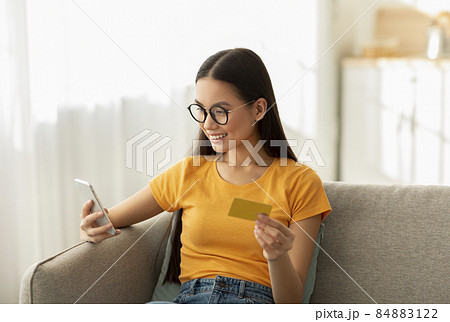 Online shopping concept. Young asian woman in glasses purchasing from home, using smartphone and credit card Online shopping concept. Young asian woman in glasses purchasing from home, using smartphone and credit card 84883122