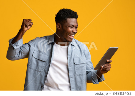 Emotional african american guy holding digital tablet and gesturing Emotional african american guy holding digital tablet and gesturing 84883452