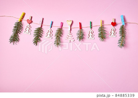 Figurines of wooden Christmas trees and fir branches are hung with clothespins on a rope on a pink background 84885339