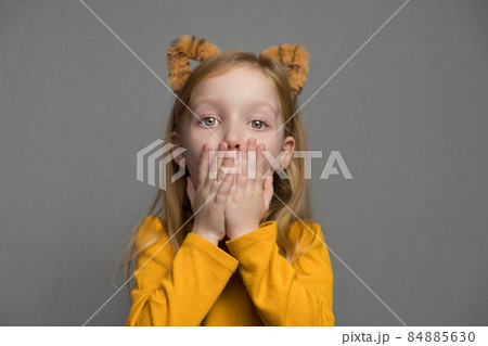 Cute surprised blond girl with tiger ears. A headdress with tiger ears. New Year 2022. Child in a tiger costume smiles sweetly and looks at camera. Cute surprised blond girl with tiger ears. A headdress with tiger ears. New Year 2022. Child in a tiger costume smiles sweetly and looks at camera. 84885630