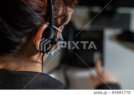 A woman call center operator in a medical mask answers the phone. A woman call center operator in a medical mask answers the phone. 84885776