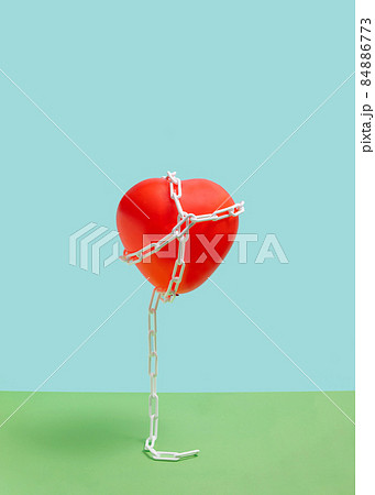 Red heart tied with a white chain on a blue and green background. 84886773