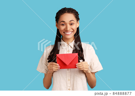 I got love letter on Valentine's day. Happy beautiful woman with black dreadlocks holding letter in red envelope or greeting card and smiling joyfully. Indoor studio shot isolated on blue background. 84888877